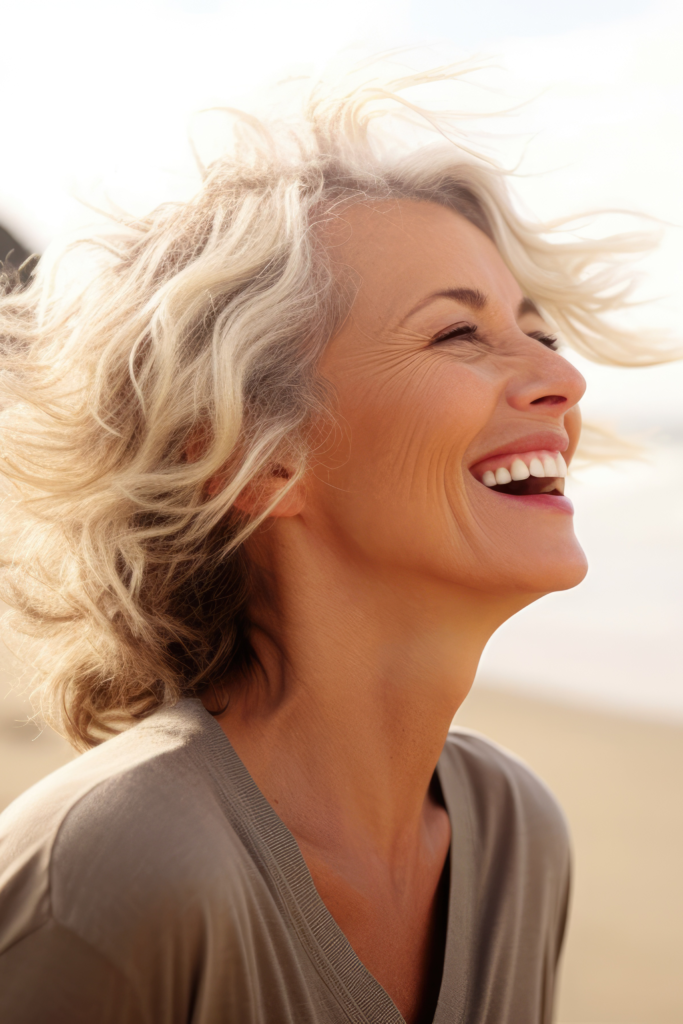 Smiling mature woman with short wavy blonde hair enjoying a sunny day outdoors, representing confidence and vitality associated with women's hormone therapy at SP Aesthetics.