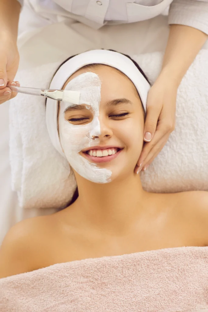 Teen girl receiving a facial treatment with a soothing mask applied, smiling and relaxed, in a spa setting, highlighting skincare and rejuvenation.